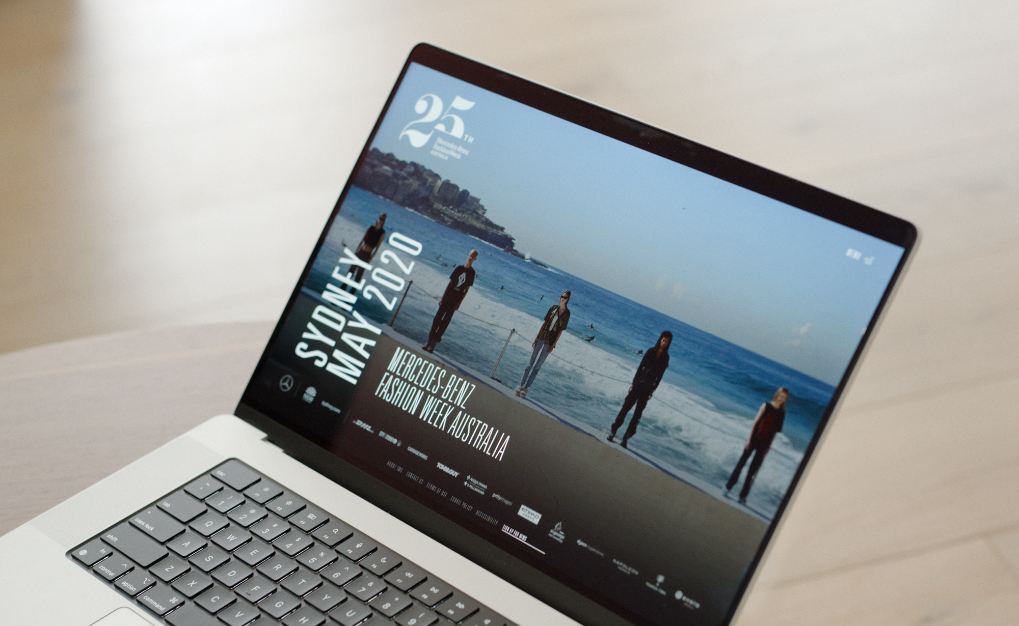 A laptop with the MBFW website showing the home page.